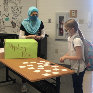 Teacher with student playing games with a mystery box on a table.