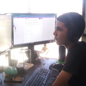 PICTURE OF SDPA ONLINE STUDENT SITTING IN FRONT OF HIS COMPUTER LISTENING TO HIS TEACHER. HAS HEADPHONES ON.