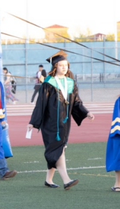SDPA student walking on grass for her graduation. Wearing a black cap and gown.