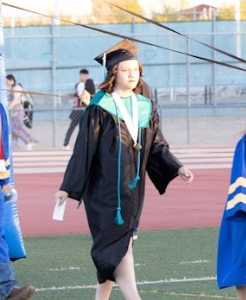 SDPA student walking on grass for her graduation. Wearing a black cap and gown.
